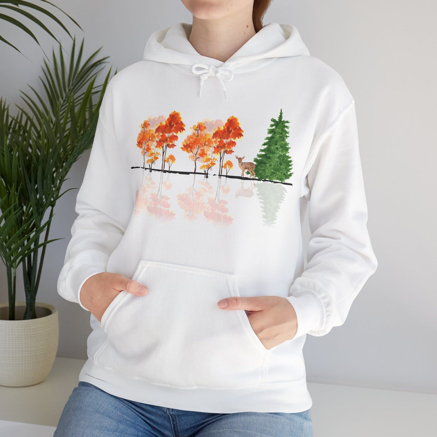 White hoodie with nature-themed design featuring trees and a deer, worn by a person.