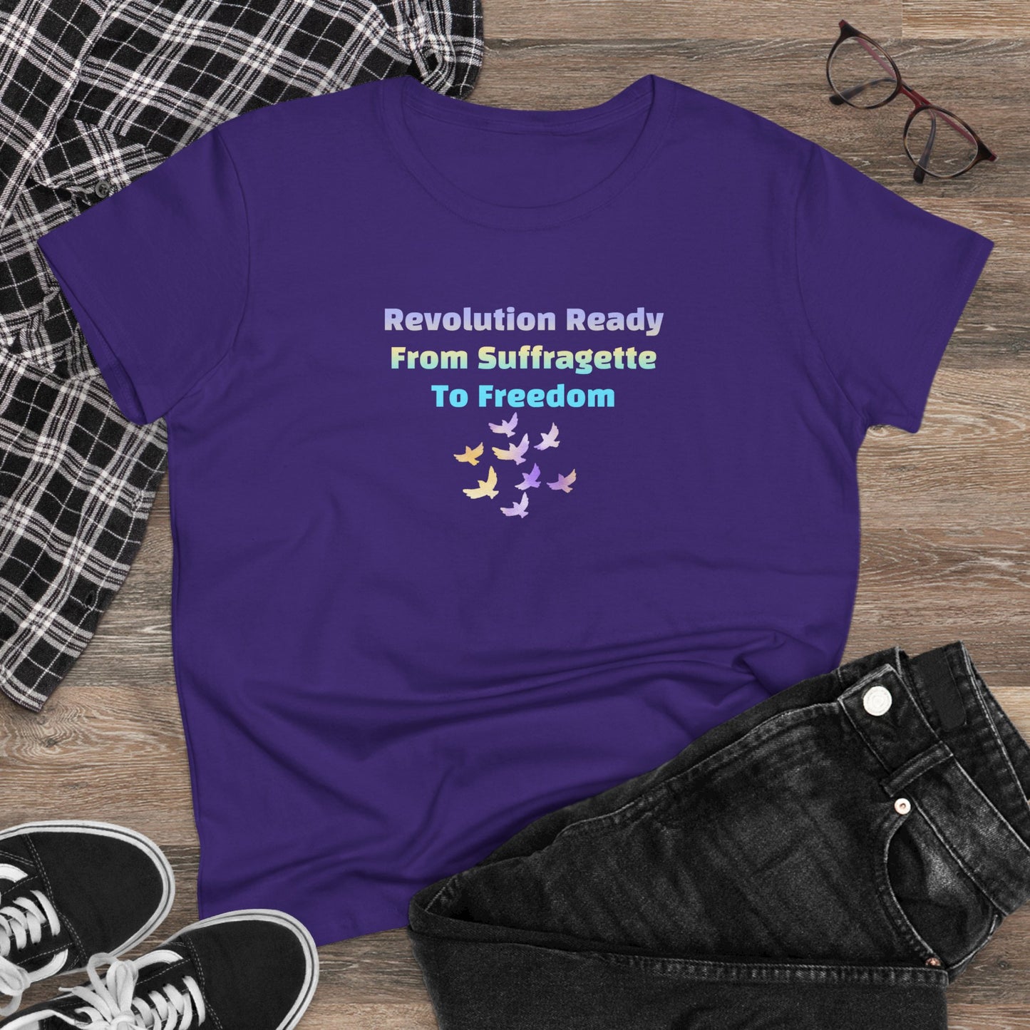 Purple t-shirt with text and doves design on a wooden surface with clothing and glasses.