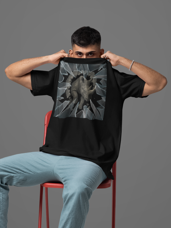 Person holding a black t-shirt with a graphic design in front of their face against a gray background