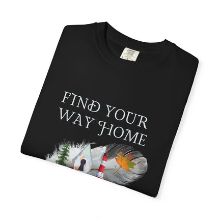 A folded black t-shirt with the text 'FIND YOUR WAY HOME' in white, featuring a graphic of a lighthouse, trees, keyhole and a leaf on a feather. 