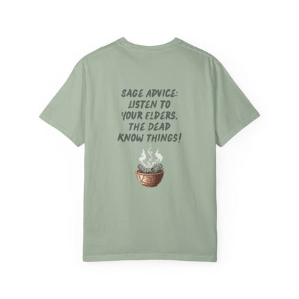 A sage green short-sleeve t-shirt with a dark gray graphic on the front reading 'SAGE ADVICE: LISTEN TO YOUR ELDERS. THE DEAD KNOW THINGS!' above a small illustration of a smoking copper cauldron containing sage, shown on a plain white background.