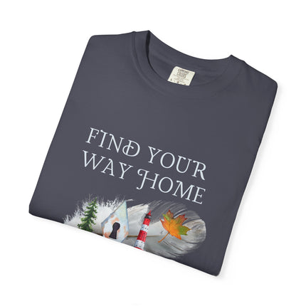 A brown crewneck t-shirt with a graphic print that reads 'FIND YOUR WAY HOME' in white serif letters above a scenic illustration of a lighthouse, a keyhole, tree, and a maple leaf. The shirt is shown folded on a clean white background.