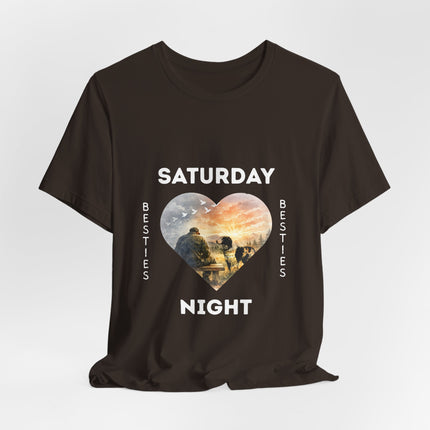A dark brown short-sleeve t-shirt with a graphic print on the front. The design features the text 'SATURDAY' and 'NIGHT' in white capital letters framing a heart-shaped illustration of veteran on a bench with his loving dog staring at him with love.
