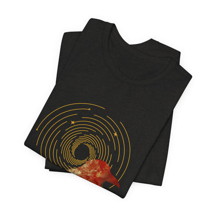 Raven dreamcatcher boho graphic with golden celestial rings and teal textured artwork on a folded black t-shirt.