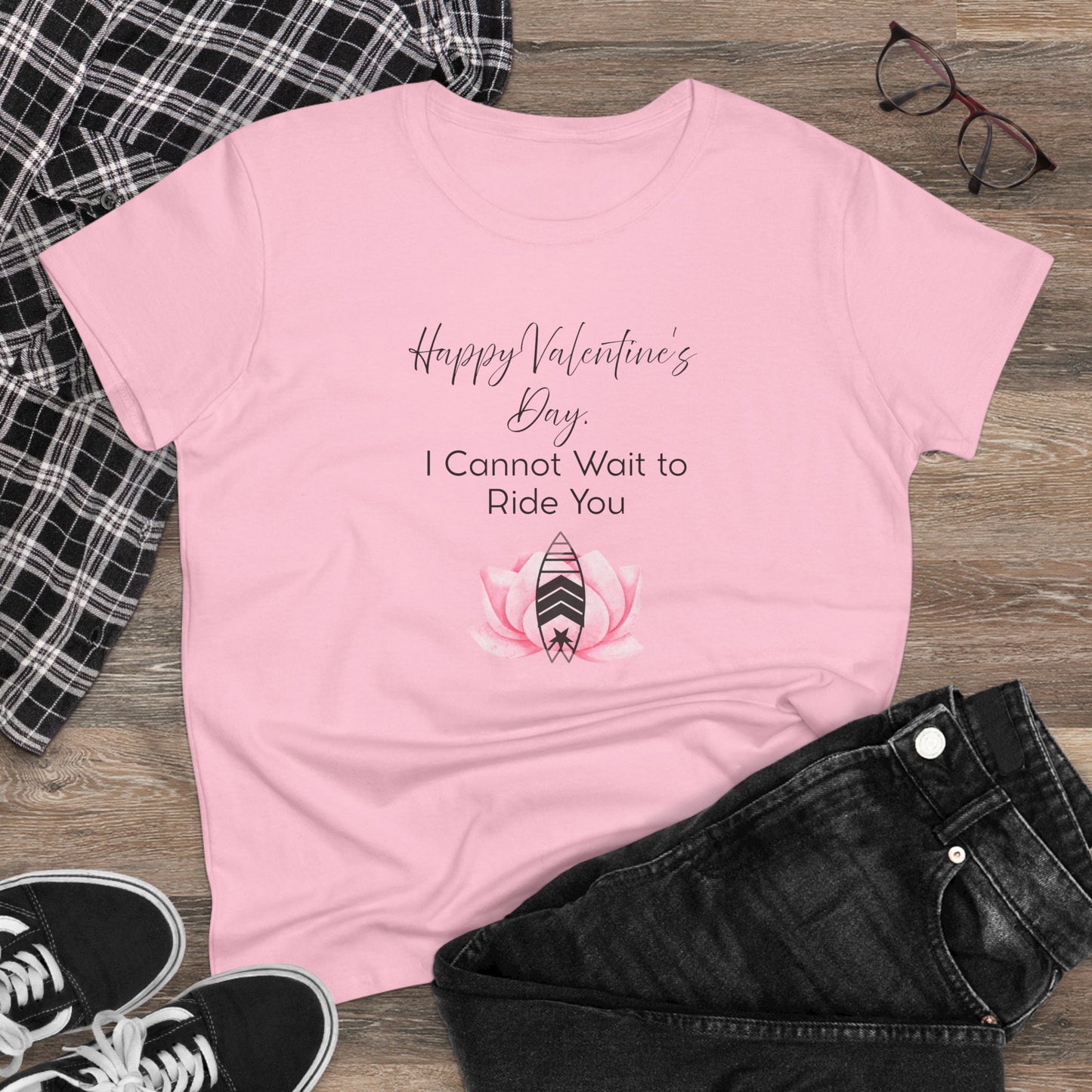 Pink t-shirt with Valentine's Day text and graphic on a wooden surface with casual items.