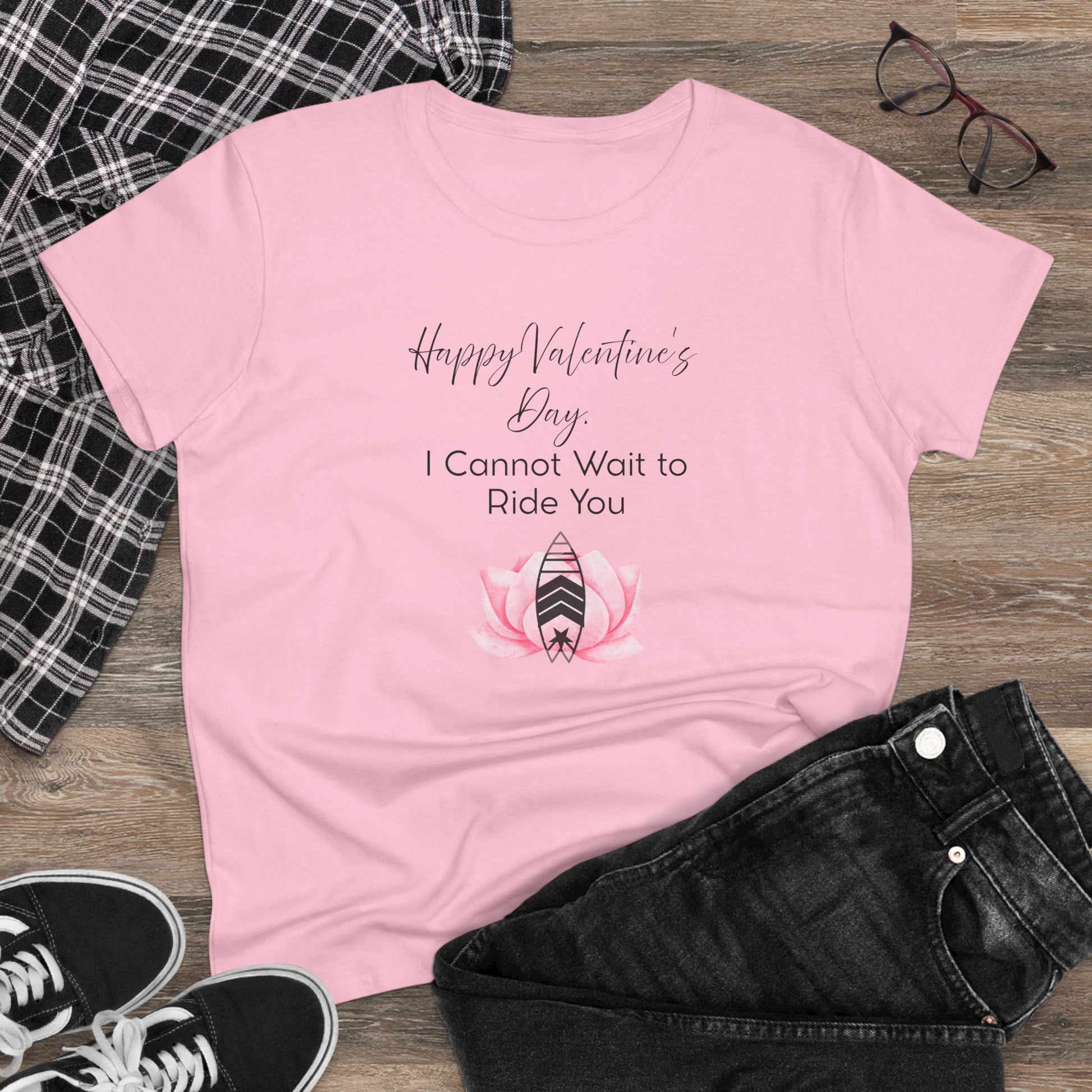 Pink t-shirt with Valentine's Day text and graphic on a wooden surface with casual items.