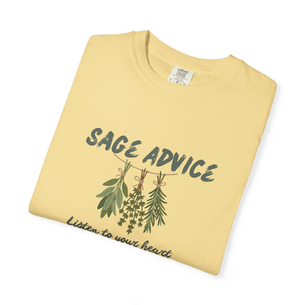 A folded pale yellow t-shirt with a graphic print of sage and other herbs hanging on a line under the text 'SAGE ADVICE' and the phrase 'Listen to your heart' in script below.