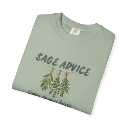A folded sage green t-shirt with a graphic print of hanging sage and rosemary sprigs under the text 'SAGE ADVICE' and the phrase 'Listen to your heart' below, shown on a plain white background.