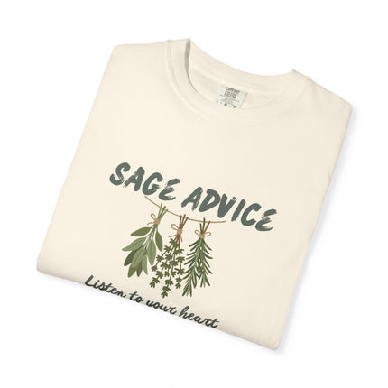 A folded cream-colored t-shirt with a graphic print of sage and herb illustrations under the text 'SAGE ADVICE' and the phrase 'Listen to your heart' in dark green script.