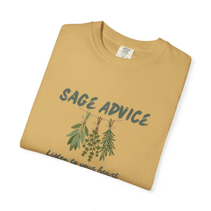A folded tan crewneck t-shirt with a graphic print of sage and thyme herbs hanging on a line under the text 'SAGE ADVICE' and the phrase 'Listen to your heart' in script, shown on a plain white background.