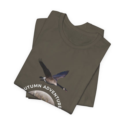A folded olive green t-shirt featuring a graphic of a flying Canada goose and the text 'AUTUMN ADVENTURE' in white, displayed on a clean white background.