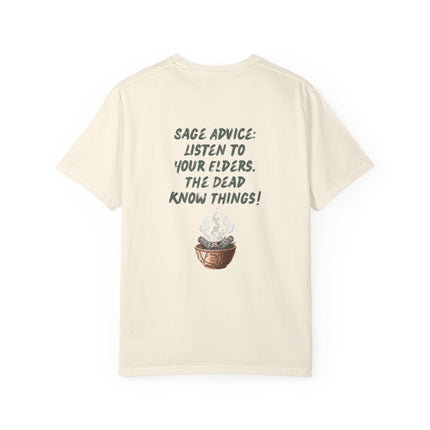 An off-white short-sleeve t-shirt with a graphic on the back featuring the text 'SAGE ADVICE: LISTEN TO YOUR ELDERS. THE DEAD KNOW THINGS!' in a dark gray font above a small illustration of a copper pot containing sage, with smoke.