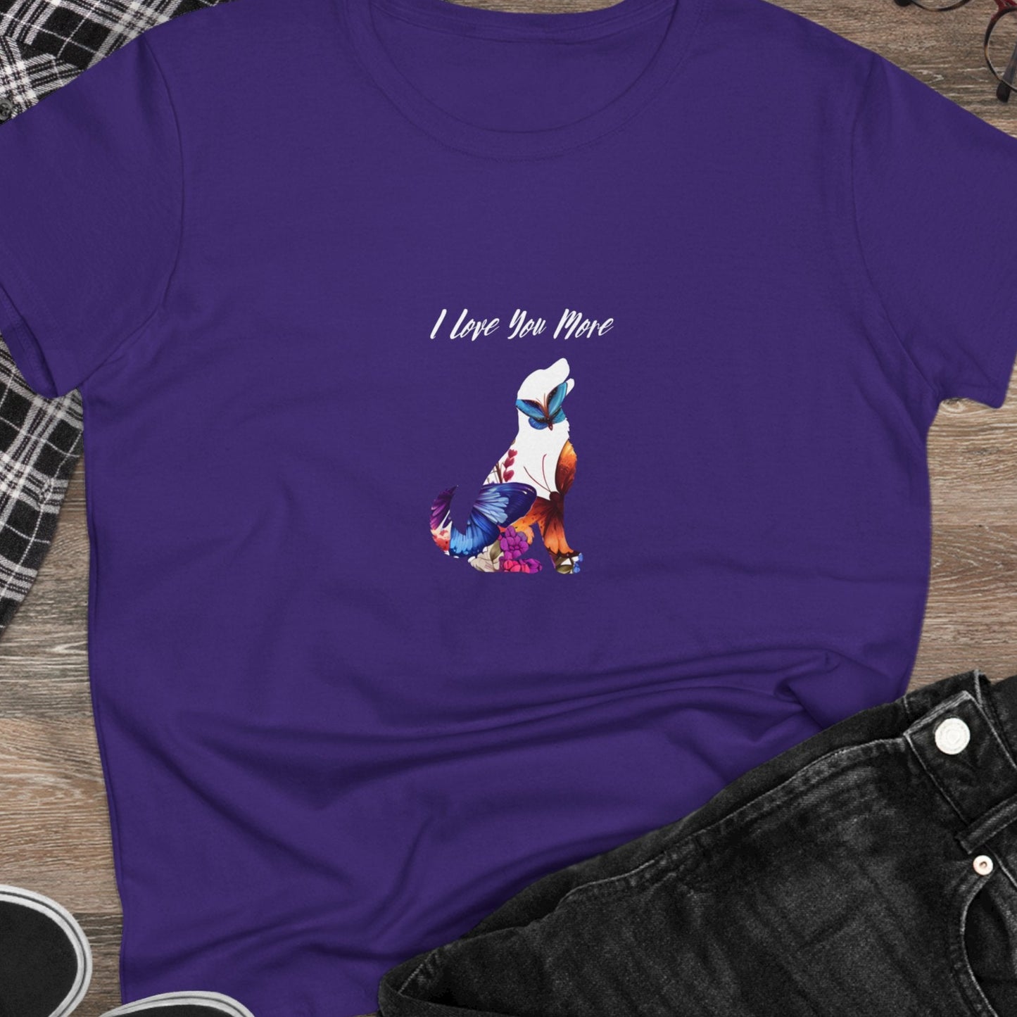 Purple t-shirt with a graphic design and text on a wooden surface with casual items.