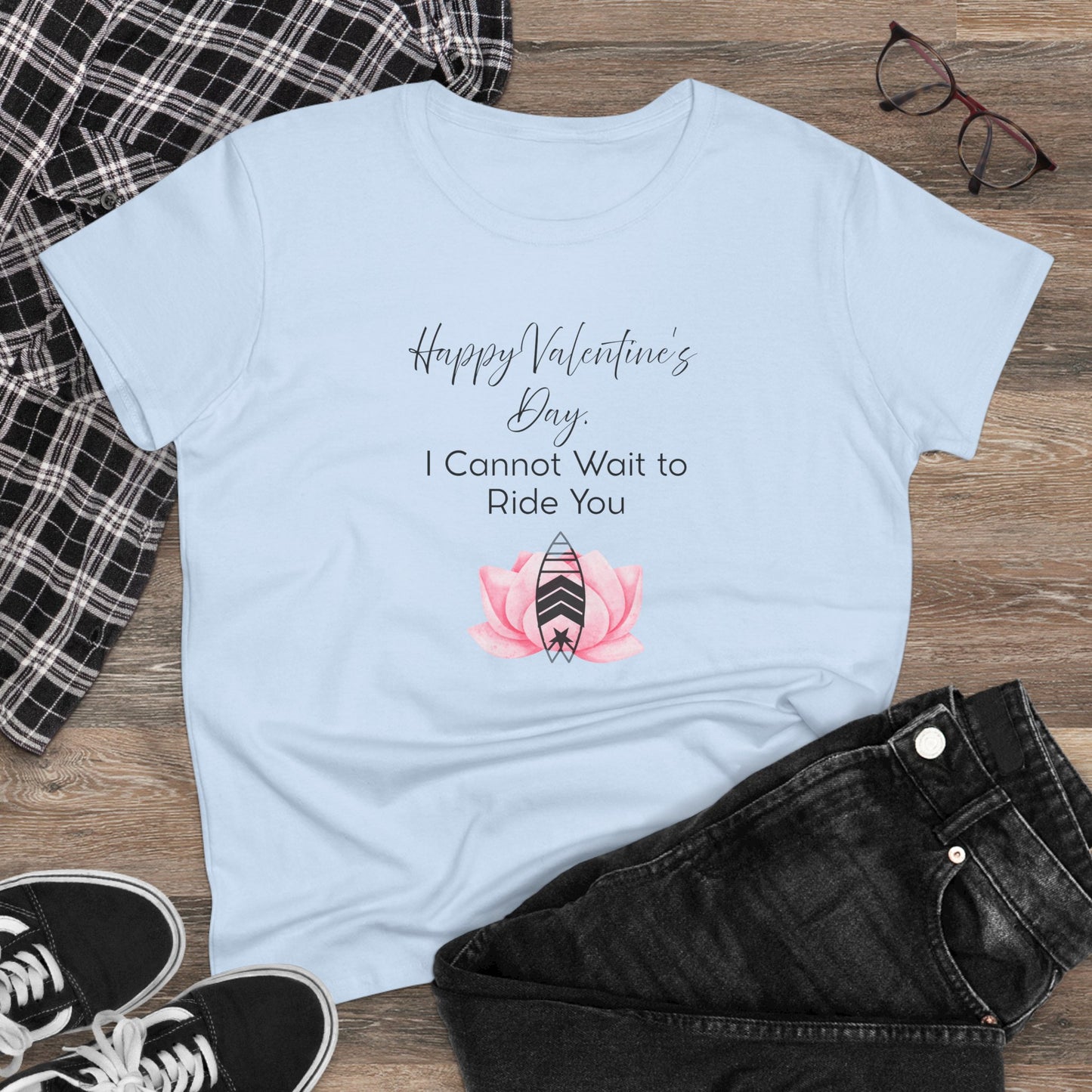 Light blue t-shirt with Valentine's Day graphic and text on a wooden surface with plaid fabric, sunglasses, and sneakers.