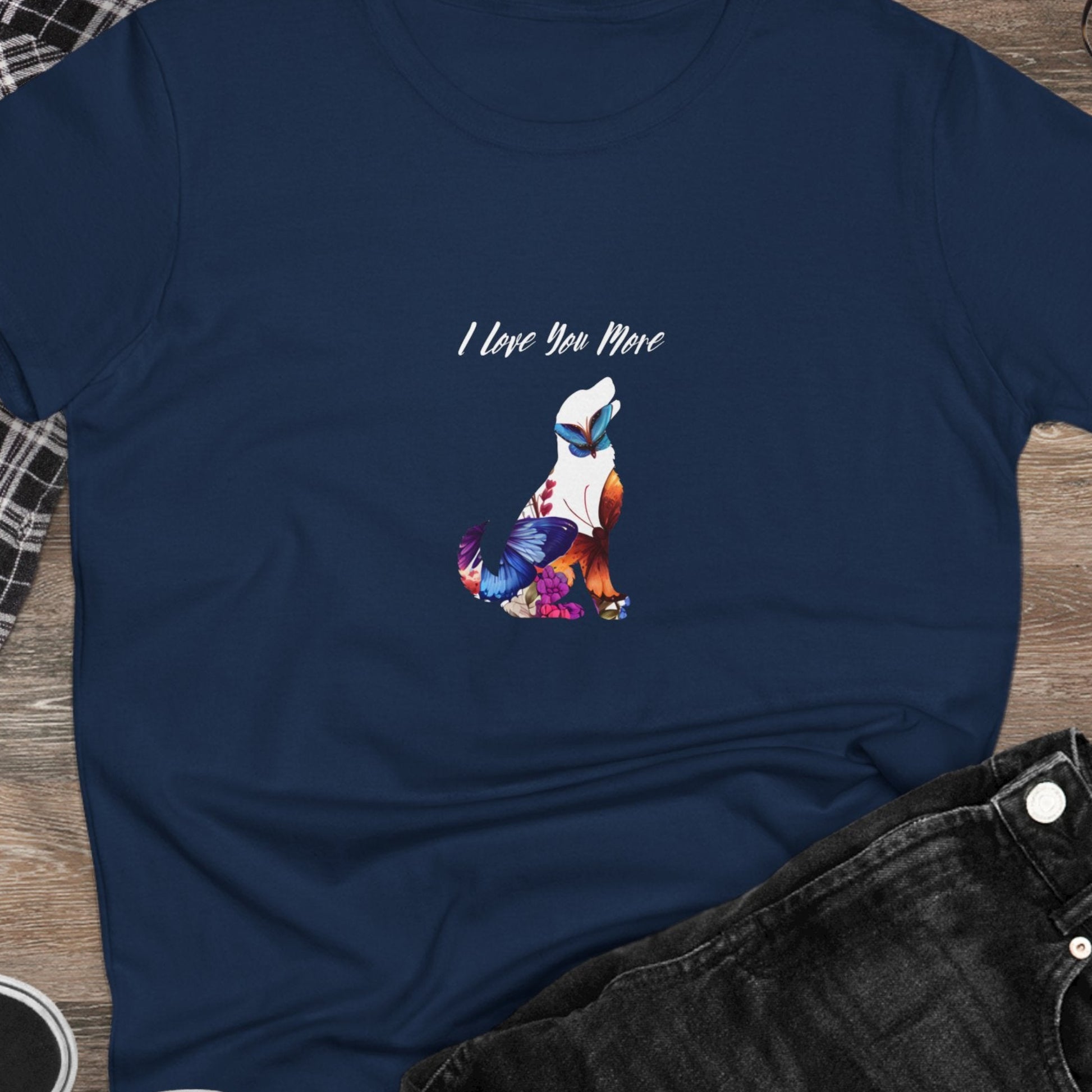 Navy blue t-shirt with colorful graphic and text 'I Love You More' on a wooden surface with casual items.