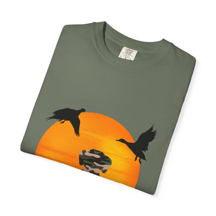 Folded green t-shirt with a graphic of ducks and a sunset on a white background