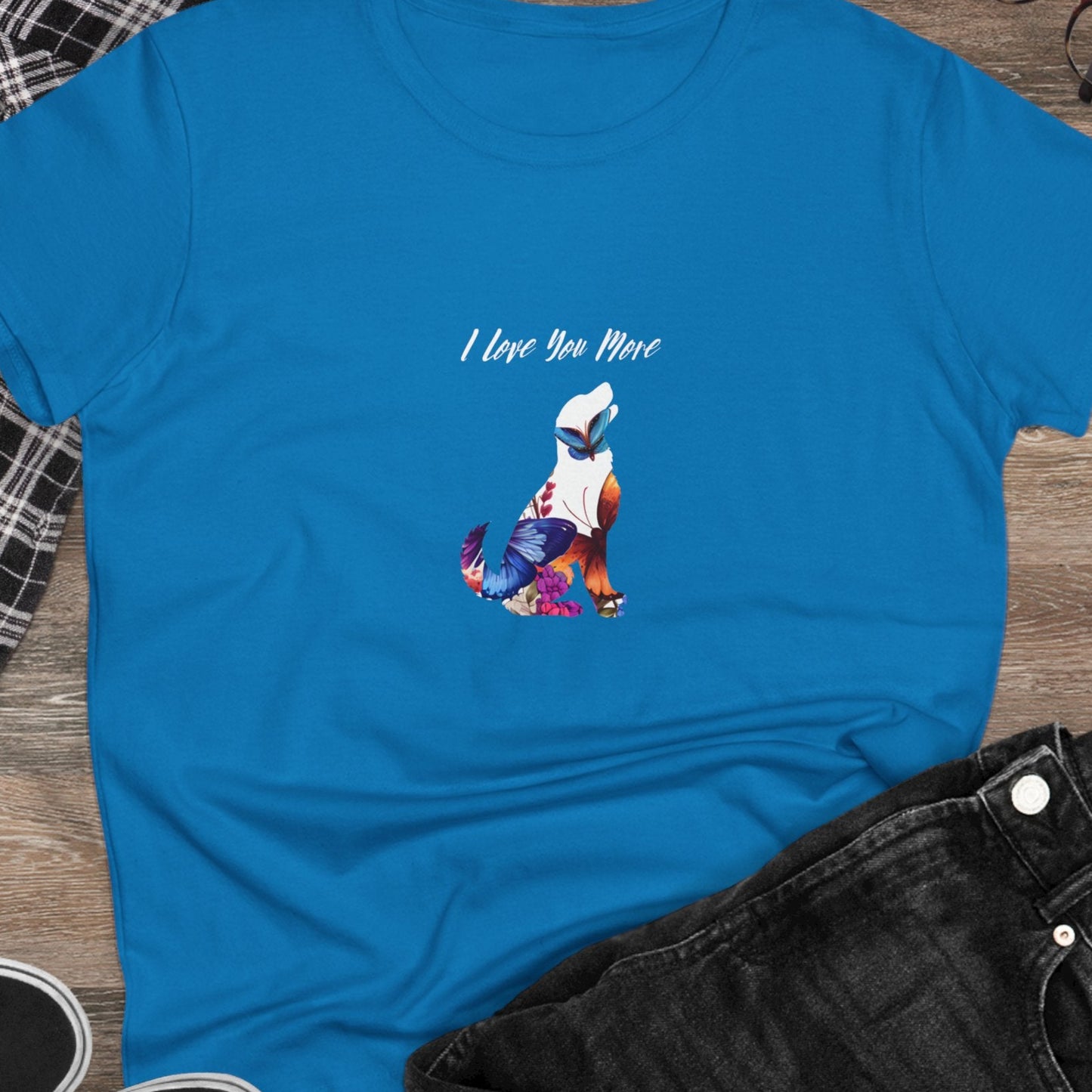 Blue t-shirt with graphic design and text on a wooden surface with casual items.