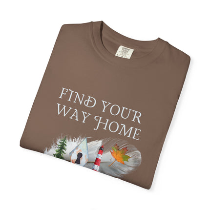 A folded brown t-shirt with the text 'FIND YOUR WAY HOME' in white, featuring a graphic of a lighthouse, trees, keyhole and a leaf on a feather. 