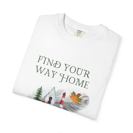 A folded white t-shirt with the text 'FIND YOUR WAY HOME' in white, featuring a graphic of a lighthouse, tree, keyhole and a leaf on a feather. 