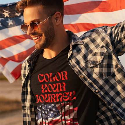 Man wearing a black t-shirt with 'Color Your Journey' text and an American flag design, standing in front of an American flag.