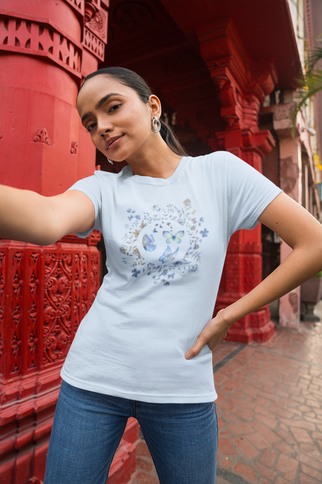 Woman wearing a light blue t-shirt with a floral design in front of red architectural elements.
