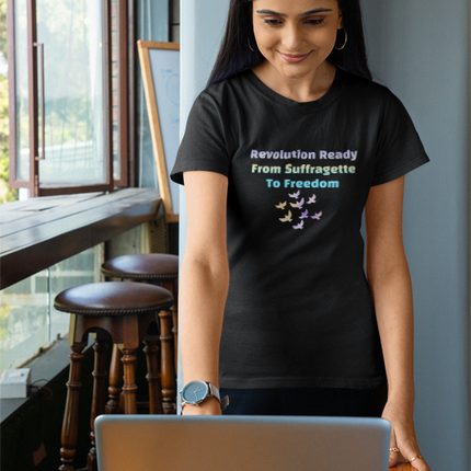 Woman wearing a black t-shirt with a colorful design and text, standing in a room with a window and wooden furniture.