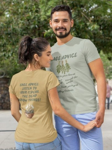 A man and a woman wearing matching sage green and tan graphic t-shirts with 'Sage Advice' text and illustrations, standing outdoors in a park-like setting.