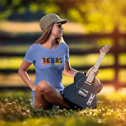 Woman with a guitar sitting on the grass wearing a blue t-shirt that says TEXAS displaying wildflowers behind the print.