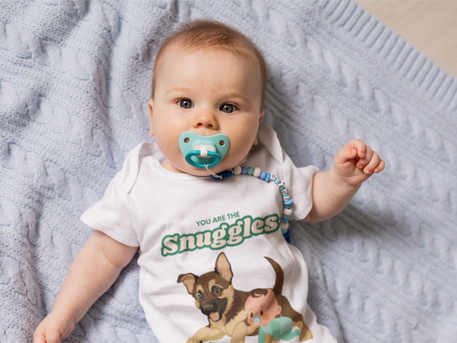 Baby wearing a onesie with a dog illustration and text, lying on a soft surface.