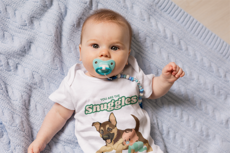 Baby wearing a onesie with a dog illustration and text, lying on a soft surface.
